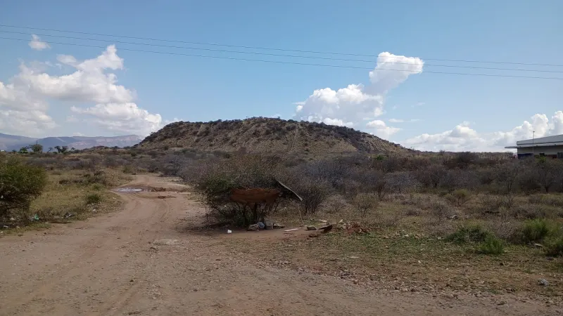 A dirt track crossing dry scrubland towards a flat-topped heap of historic mine waste, under a blue sky.